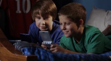 两小孩趴在床上一起打游戏机视频素材